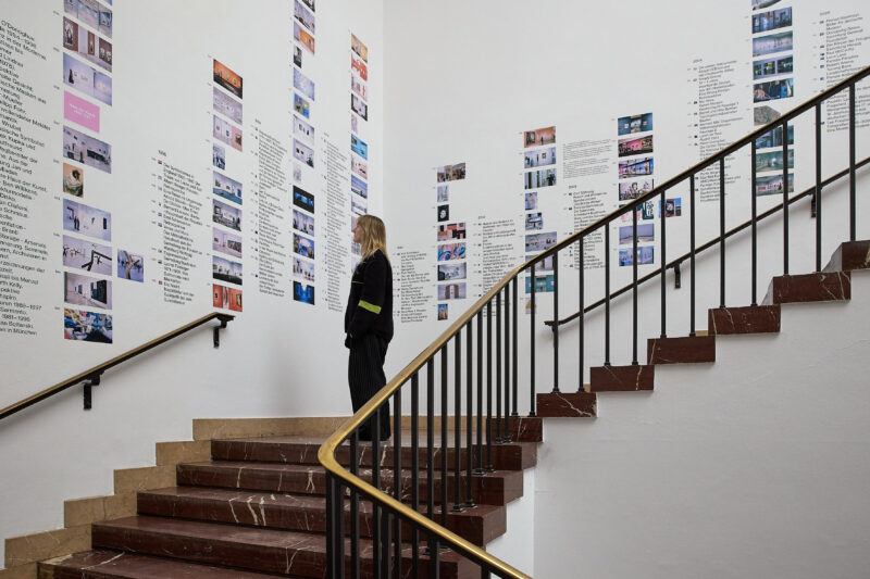 Eine Person steht auf einer Treppe und schaut sich kleine Bilder an den Wänden an.
