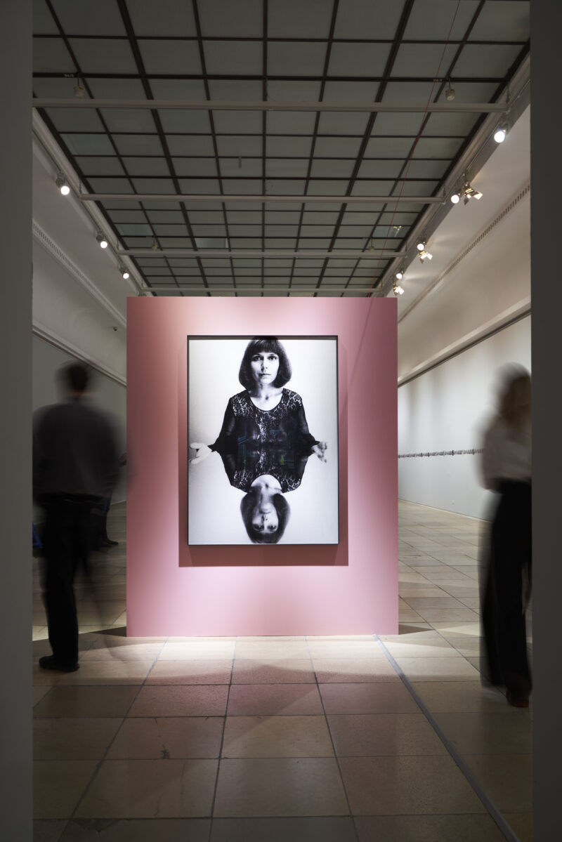 Eine rosa Aufstellwand mit einem großen Portrait Katalin Ladiks.