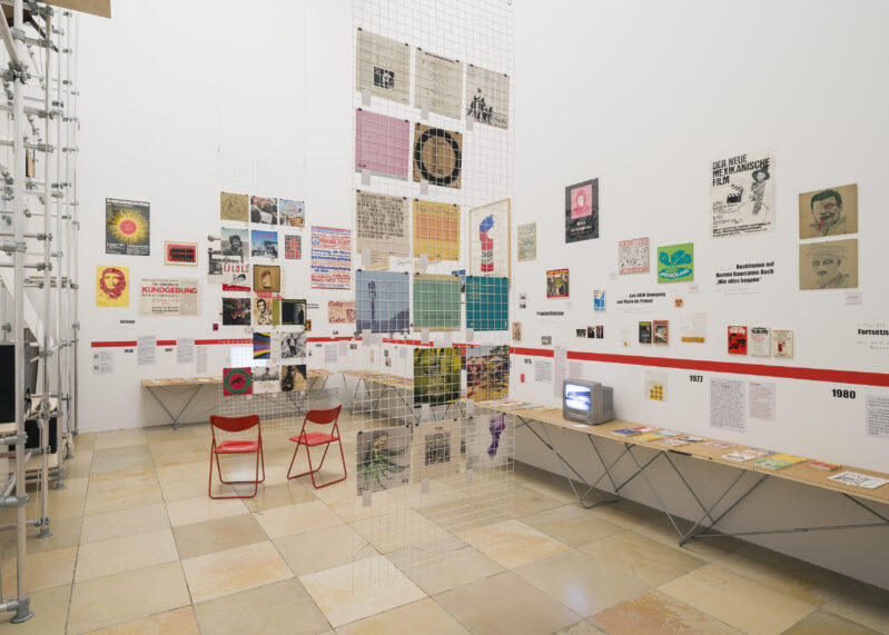 Der Ausstellungsraum ist voller Archivalien, Fotos, Postern, Büchern, die hängen und liegen.
