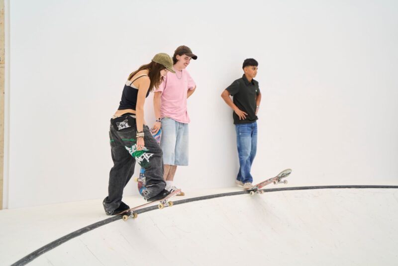 An der Kante einer weißen Skaterampe stehen drei jugendliche Personen.