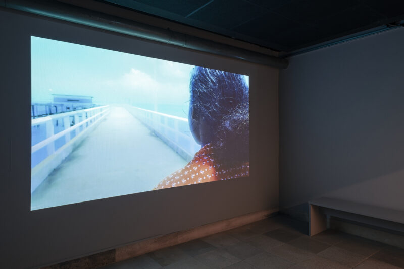 Auf die Wand wird ein Film projiziert, darin eine Frau auf einer Brücke.
