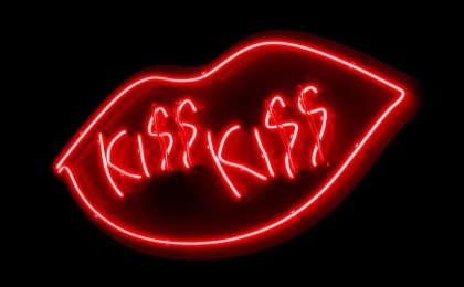 Auf schwarzem Grund befindet sich ein Kussmund aus roten Neonlichtröhren und der Schriftzug "KISS KISS".