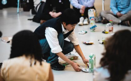 Eine Person sitz auf dem Boden währedn viele andere um sie herum sitzen.