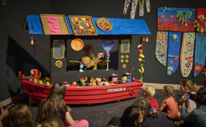 Kinder sitzen vor einem Puppetheater, das aussieht wie ein Schiff.