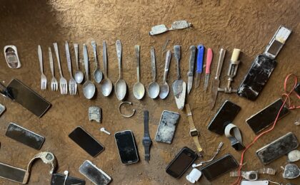 Auf einem erdigen Boden liegen mehrere verrostete Gegenstände.