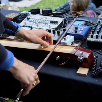 Zwei Hände spielen ein Streichinstrument, welches auf einem Tisch liegt.