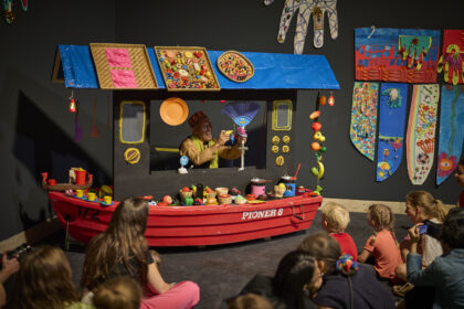 Kinder sitzen vor einem Puppetheater, das aussieht wie ein Schiff.