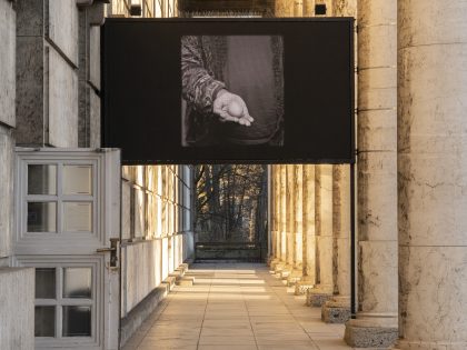 Ein Bildschirm mit Videofilm zwischen Säulen auf der Terrasse.