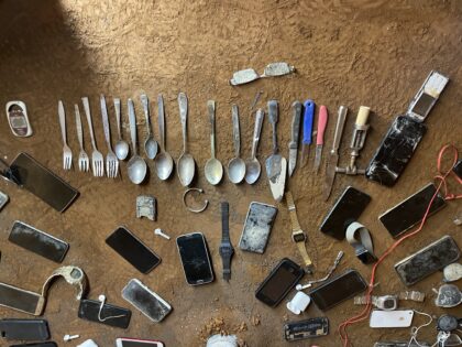 Auf einem erdigen Boden liegen mehrere verrostete Gegenstände.