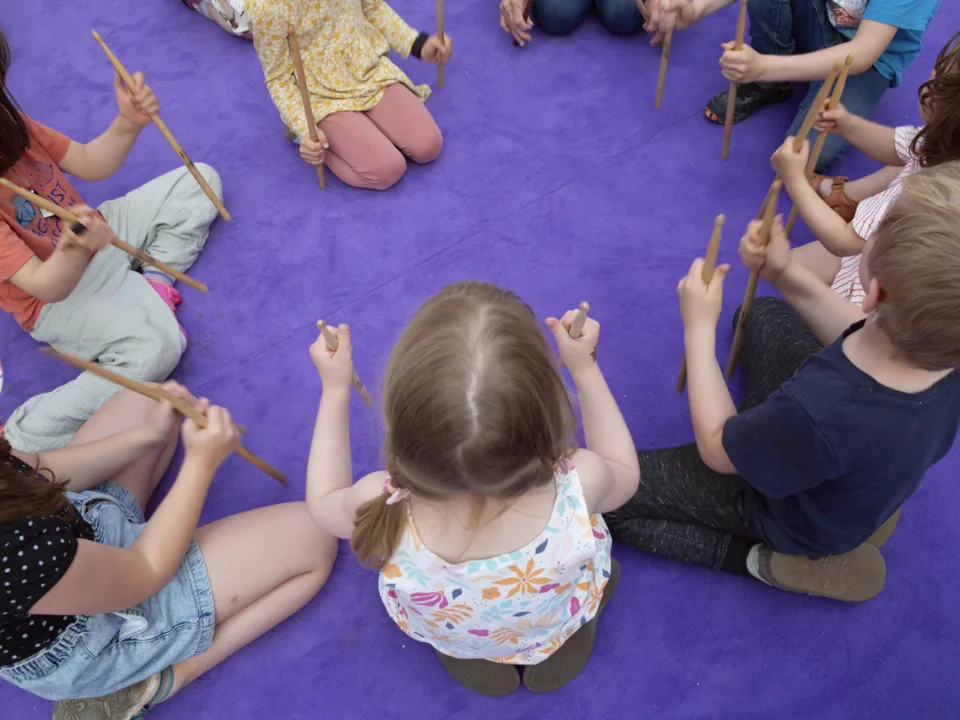 Kinder sitzen auf einem lilanen Teppichboden.