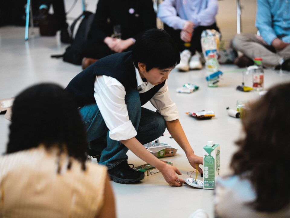 Eine Person sitz auf dem Boden währedn viele andere um sie herum sitzen.