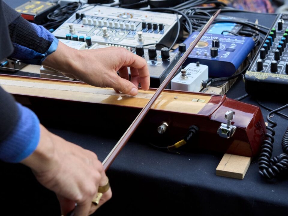Zwei Hände spielen ein Streichinstrument, welches auf einem Tisch liegt.