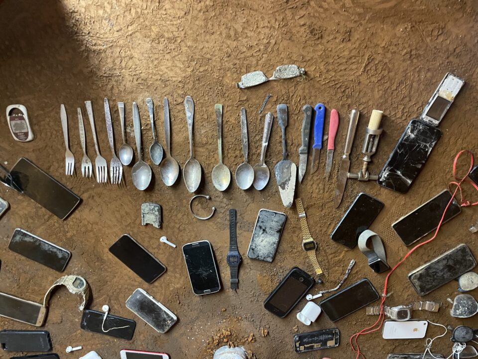 Auf einem erdigen Boden liegen mehrere verrostete Gegenstände.